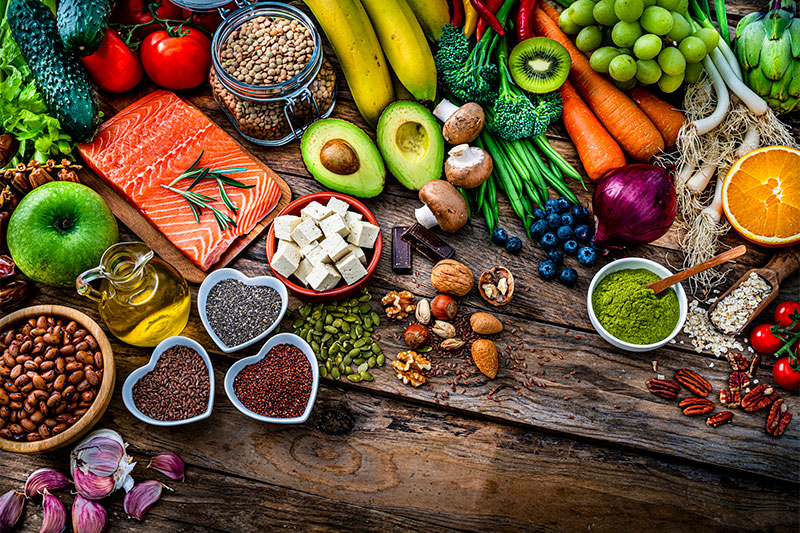 A large assortment of healthy vegetables, fruits, and grains on top of a wooden table top