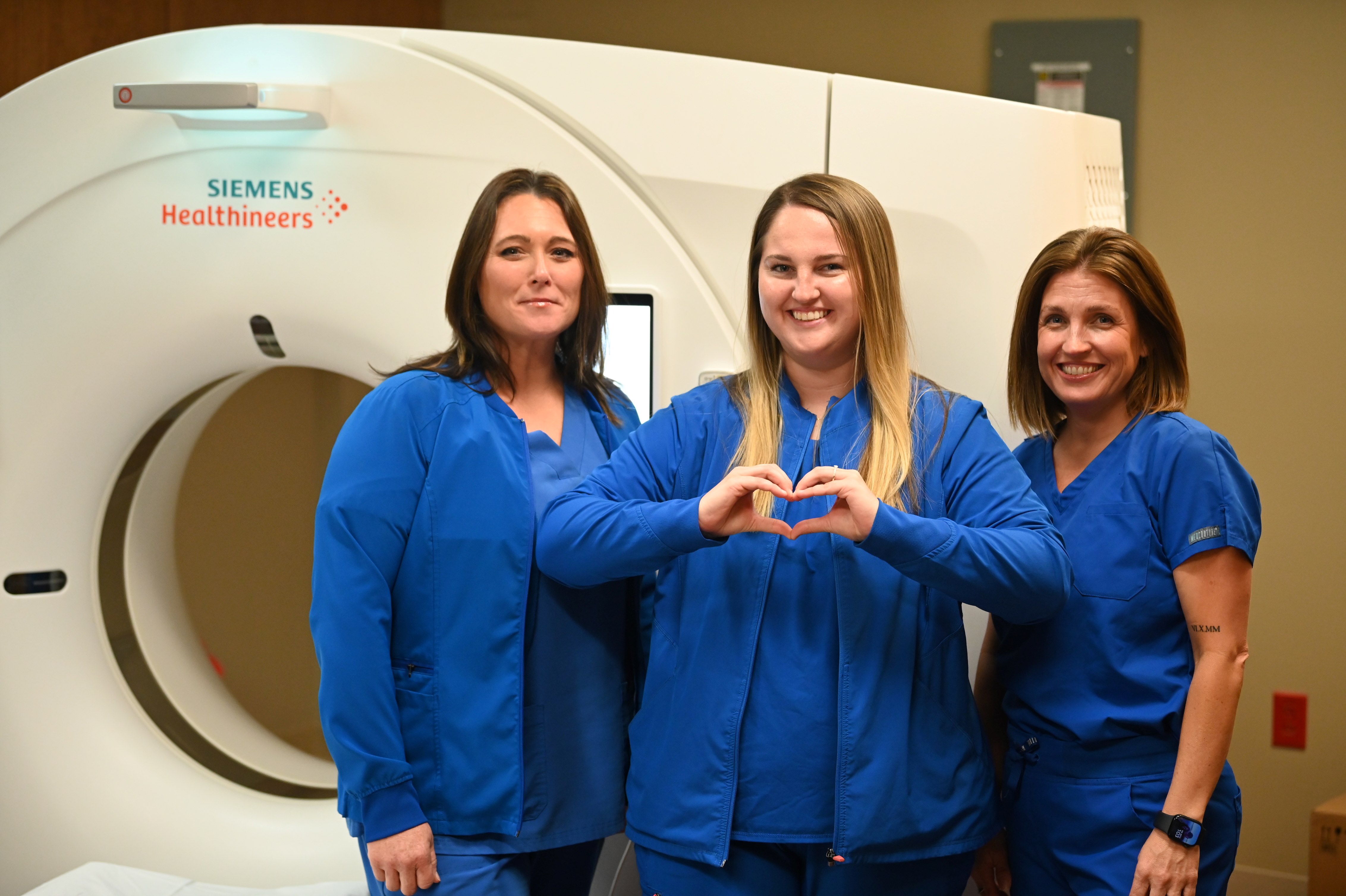 Three radiology technologists stand in front of a CT scanner