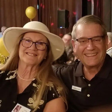 Charles, sitting with his wife, is smiling at the camera.