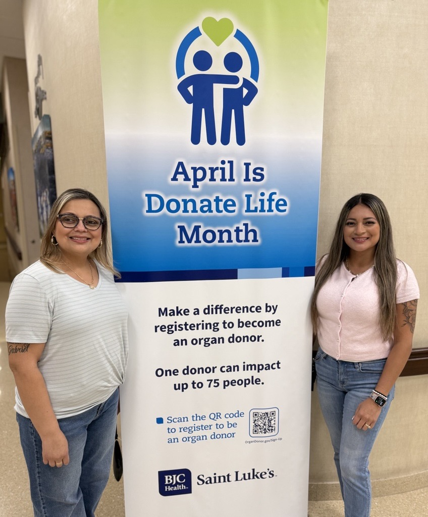 Daisy and Illena wearing white top and blue jeans, standing near a St. Luke's Donate Life Month sign