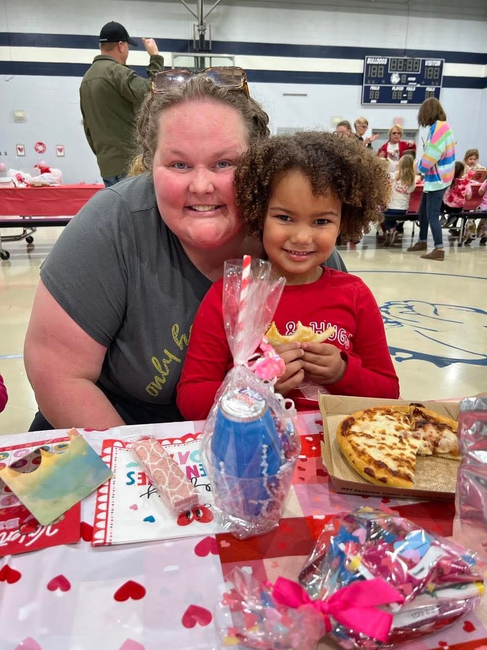 Elizabeth poses with her daughter Zakiyah, who is sitting at a table in a gym with other children and parents