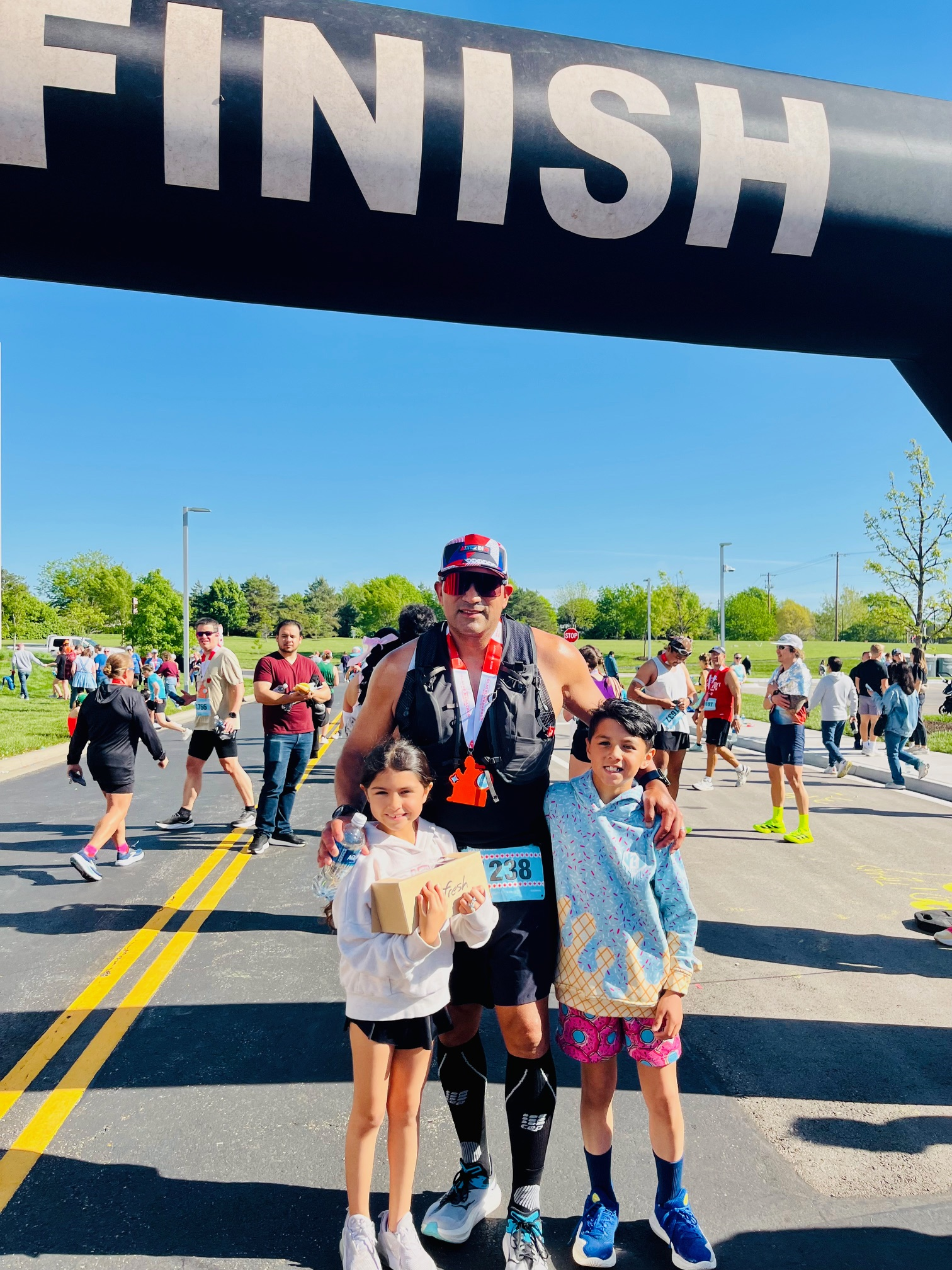 Richard Trujillo wearing a tank, shorts and standing in front of a Finish line, posing with his two daughters