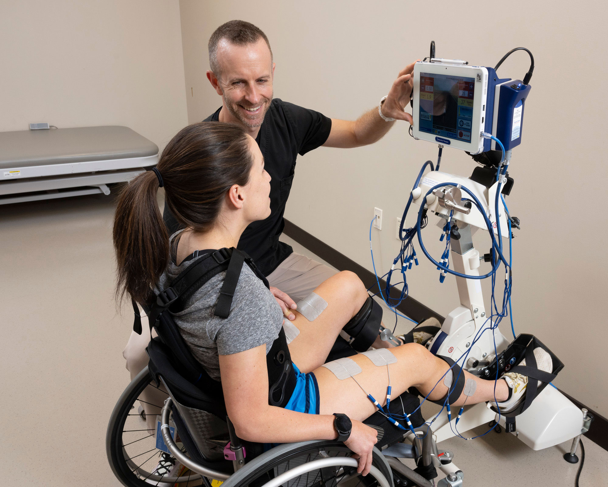 Therapist smiles with patient doing stationary bike stimulation therapy